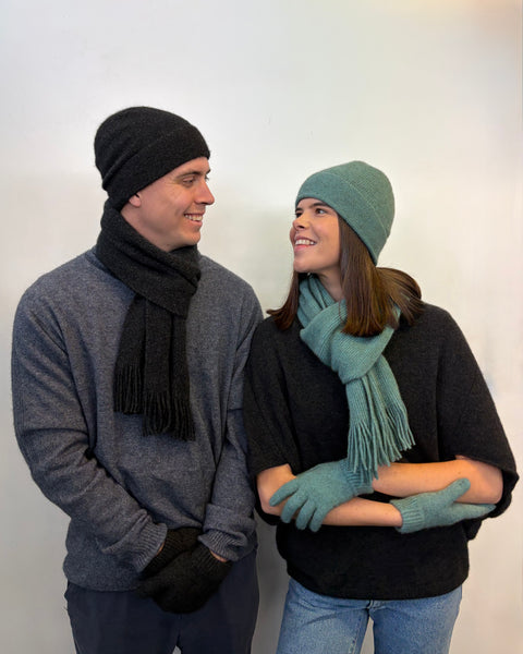 Two people wearing winter clothing including hats, scarves, and gloves against a white background.