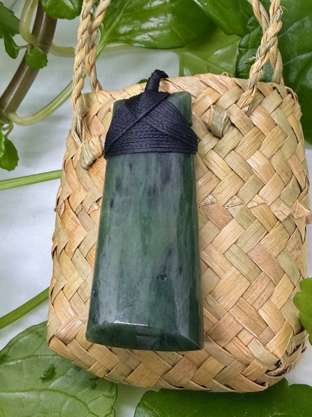 Greenstone pendant with a bound black cord on a woven flax bag
