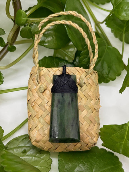 Greenstone pendant with a bound black cord on a woven flax bag