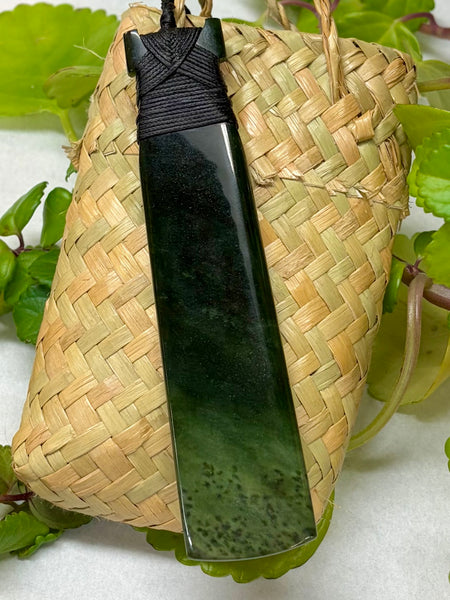 Greenstone pendant with a black cord on a woven flax bag