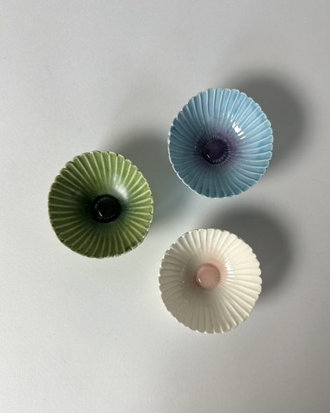 Three unique small ceramic handcrafted gerbera flower bowls in green, blue, or pink. Made in New Zealand by Muddy Fingers and sold individually.