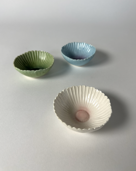 Three unique small ceramic handcrafted gerbera flower bowls in green, blue, or pink. Made in New Zealand by Muddy Fingers and sold individually.