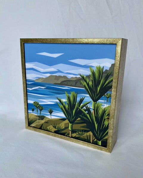 Framed artwork of a tropical landscape with palm trees and a blue sky.