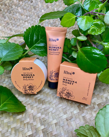 Hive Manuka Honey skincare products on a woven surface with green leaves.