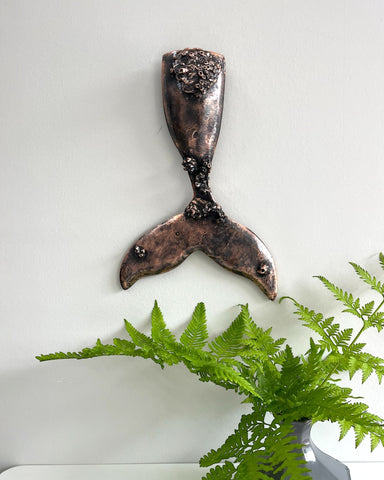 Decorative copper whale tail wall art with preserved barnacles.