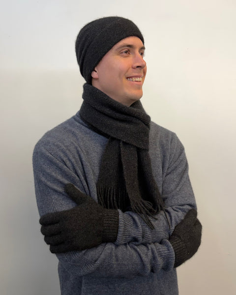 Man wearing a grey sweater, black beanie, scarf, and gloves against a white background
