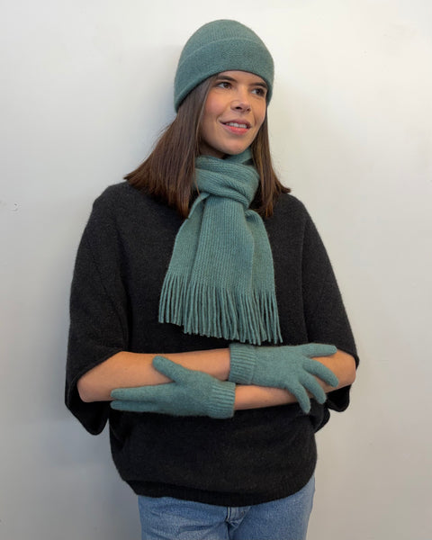 Person wearing a teal beanie, scarf, and gloves against a white background