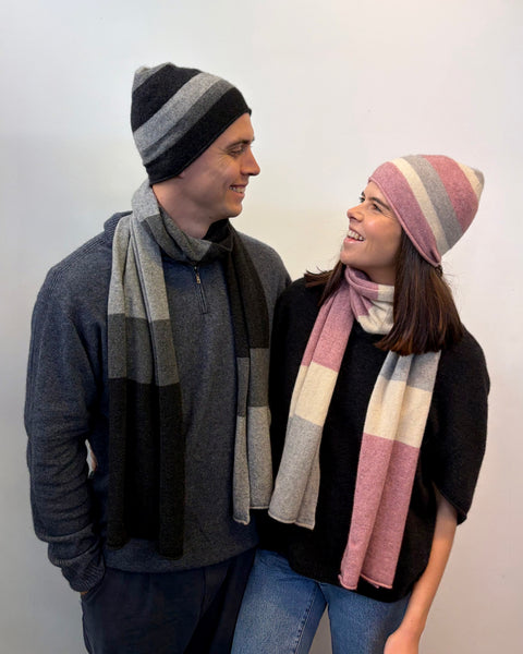 Two people wearing striped beanies and scarves against a plain background