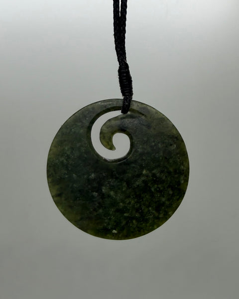 A round Greenstonr pendant with a spiral cutout, suspended from a black cord against a light grey background.