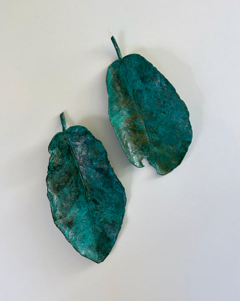 Two decorative copper electroplated Puka leaves with a green patina finish, displayed on a white background.