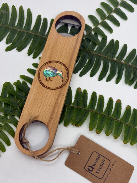 Wooden bottle opener with a kiwi bird design on a white background with green leaves.