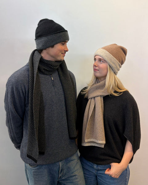 Two people wearing scarves and beanies against a plain background