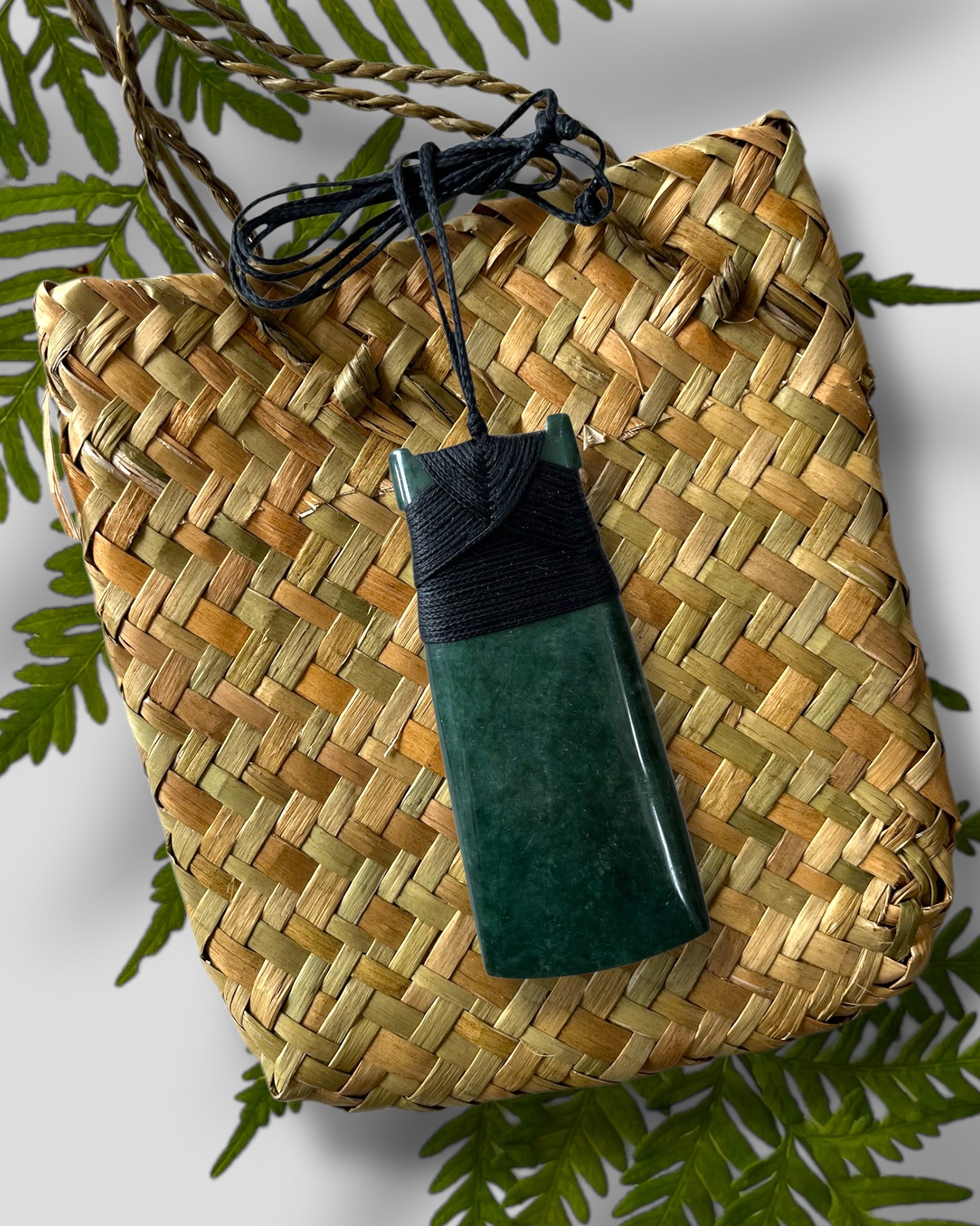 New Zealand Greenstone Pounamu Toki pendant with a black handwoven cord, presented with a flax kete bag. 