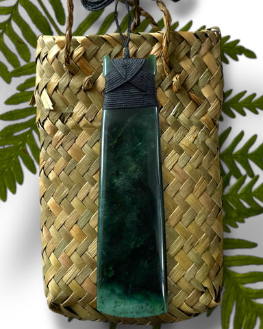 Long New Zealand Greenstone Toki pendant with a black handwoven cord, presented with a flax kete bag. Pounamu sourced from South Island Aotearoa. Hand carved by Master Carver in Greymouth.