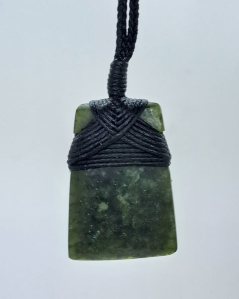 A greenstone pendant with a black cord woven around the top.