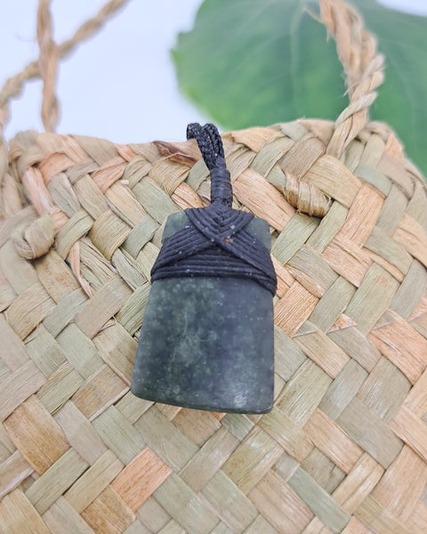 A greenstone pendant with a black woven cord.