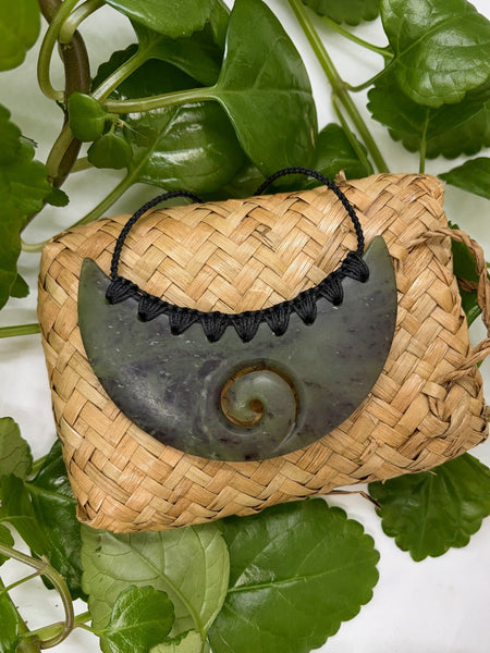 Greenstone breastplate necklace with a spiral carving on a woven flax bag