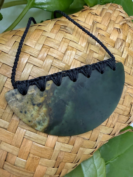 Greenstone breastplate pendant with a bound black cord on a woven flax bag