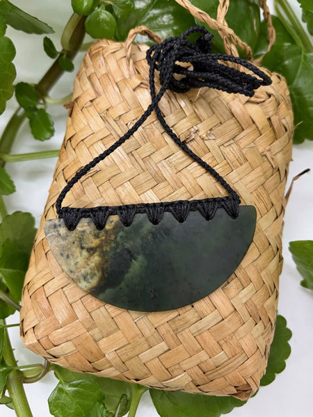 Greenstone breastplate necklace with bound black cord on a woven flax bag
