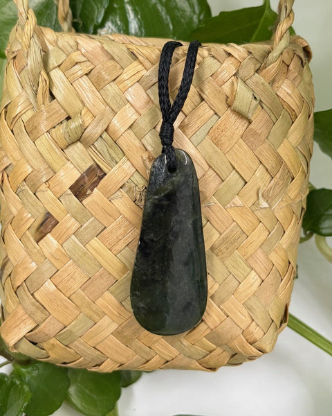 Greenstone teardrop pendant with a black cord on a woven flax bag