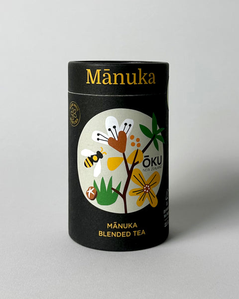 A package of OKU Manuka Blended Tea featuring a black label with a colorful illustration of native New Zealand plants and a bee, indicating the natural ingredient Manuka Leaf.