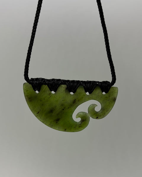 A carved greenstone pendant necklace with a black braided cord, featuring a Māori koru design, shown against a neutral gray background.