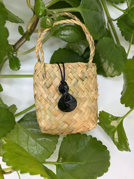 Greenstone pendant with a black cord on a woven flax bag.