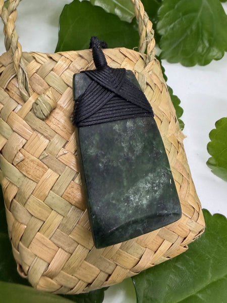 Greenstone pendant with bound black cord on a woven flax bag