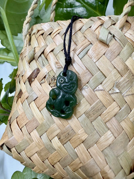Greenstone tiki pendant with a black cord on a woven flax bag