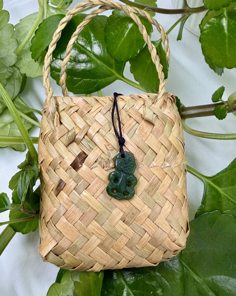 Greenstone tiki pendant with a black cord on a woven flax bag