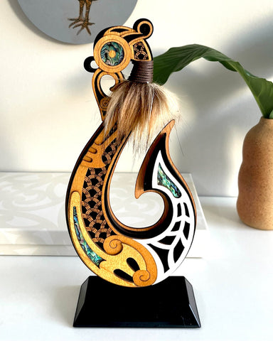 A New Zealand Made contemporary wooden art sculpture of Maui's fish hook with traditional Maori design elements and NZ Paua shell embellishments
