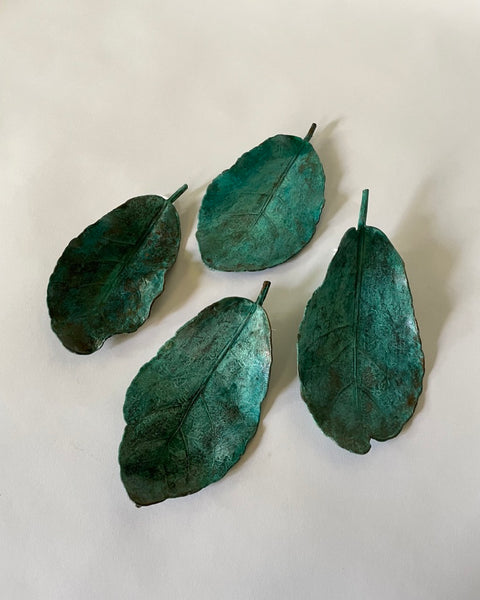 A collection of electroplated, patinated copper puka leaves on a white surface. 